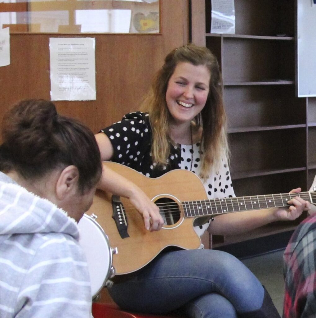 Laura Halligan Music Therapist smiles while playing guitar