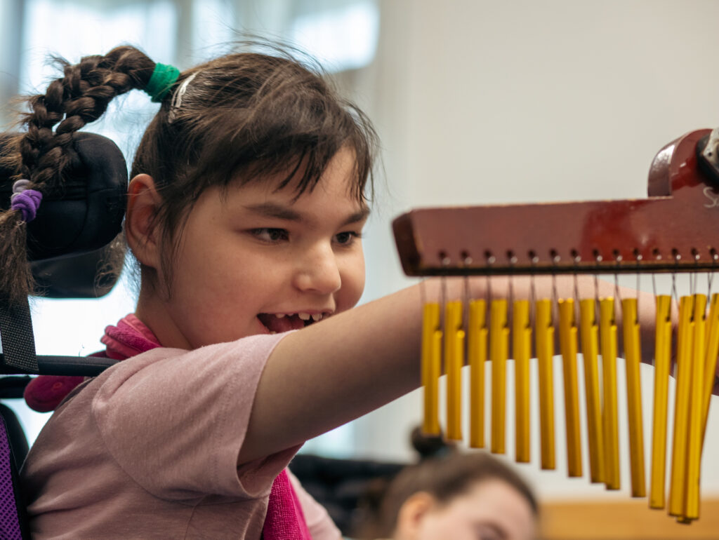 A young person plays the chimes and is smiling